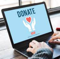 Close-up of a woman using a laptop with a donation screen displayed, showing the word “DONATE” above a heart and hands graphic, encouraging online charitable contributions.